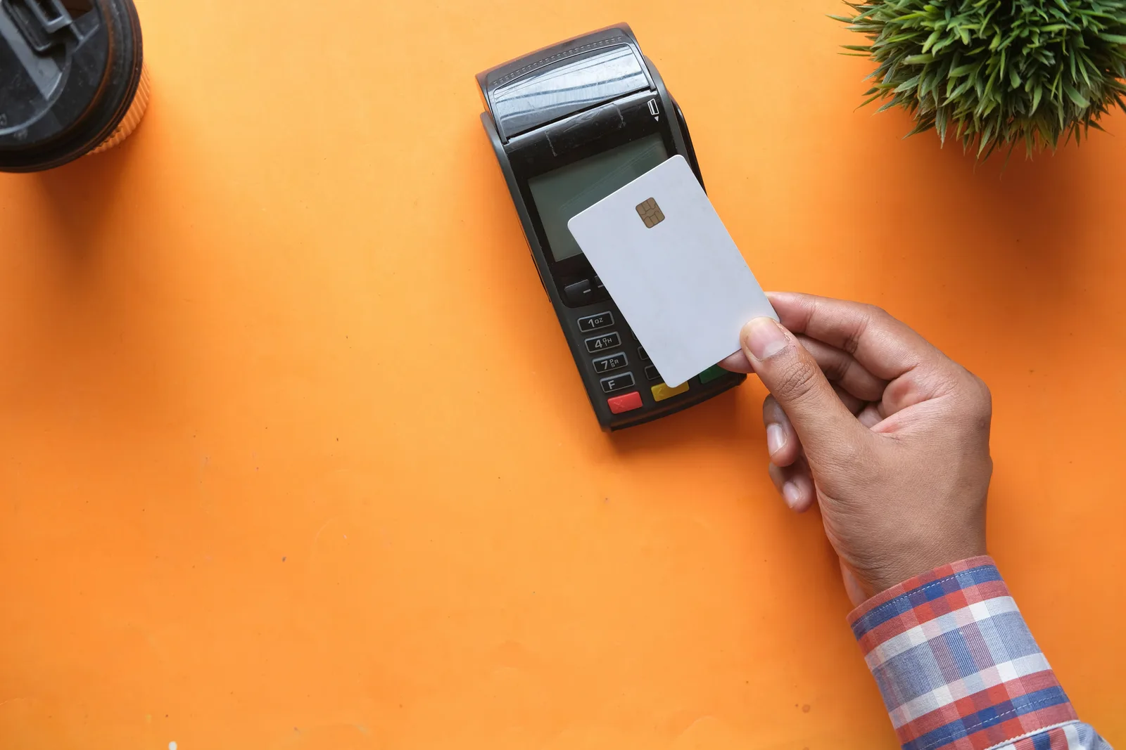 Hand houdt een betaalkaart tegen een pinautomaat op een oranje tafel