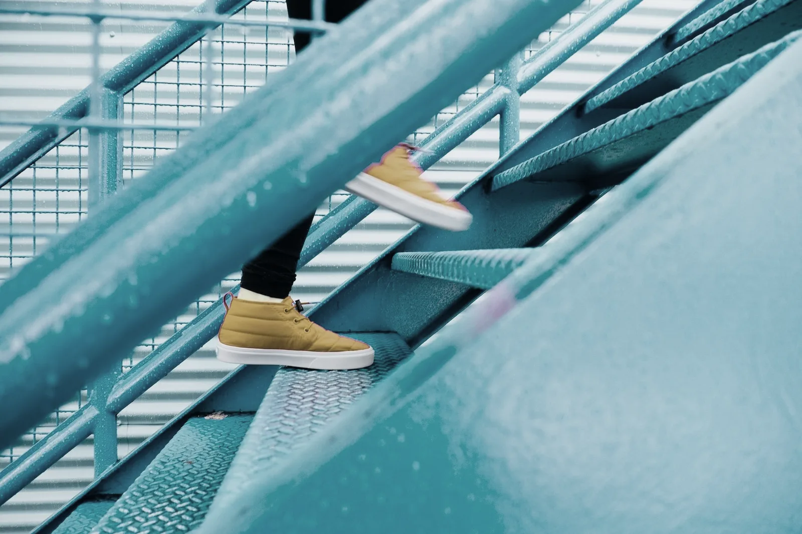 Iemand in gele sneakers loopt een teal stalen trap op